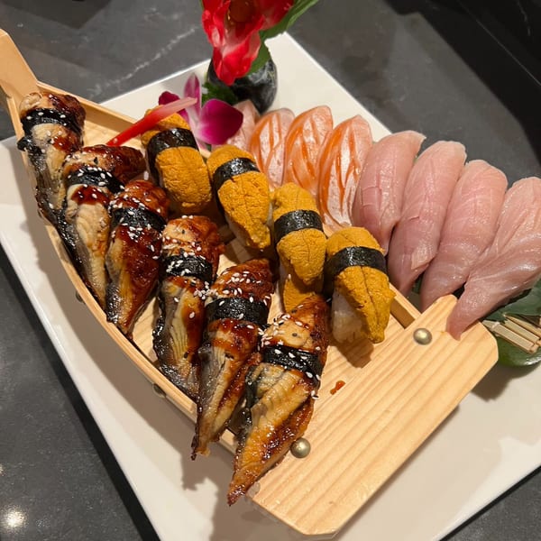 A wooden boat filled with various sushi and sashimi, including eel, uni, salmon, and tuna.