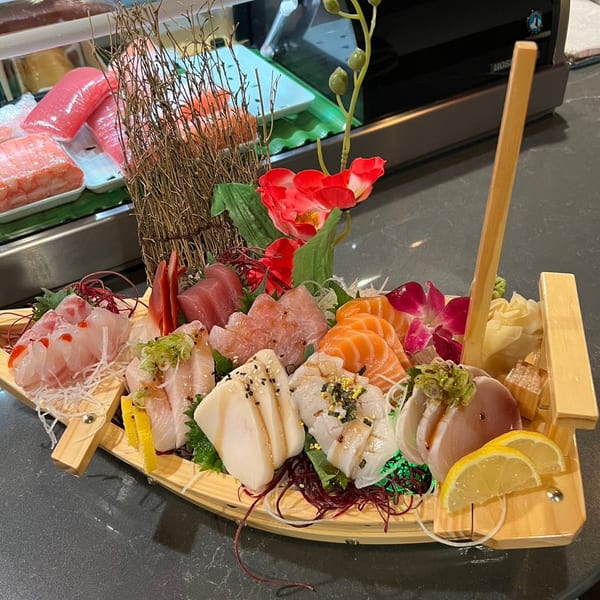 A wooden boat filled with various sashimi, including salmon, tuna, and white fish, garnished with lemon and flowers.