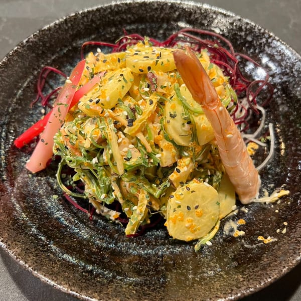 A vibrant Asian salad with shrimp, seaweed, and yellow slices, garnished with red strands and sesame seeds.